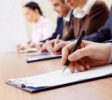 Row of business people making notes with focus on hand holding pen